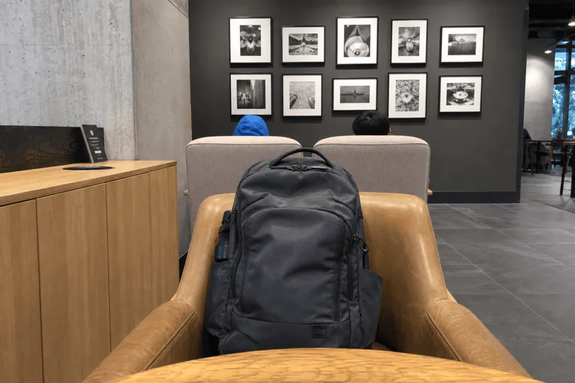 Camera view from a MacBook on a café table, with a backpack on the chair opposite.